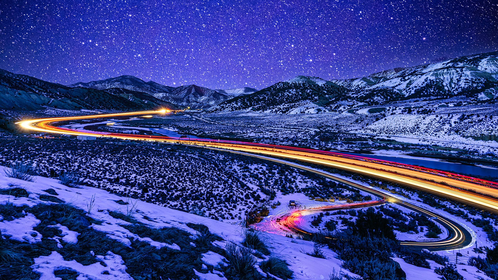 Snowy mountains with a highway, illuminated in yellow and red light.