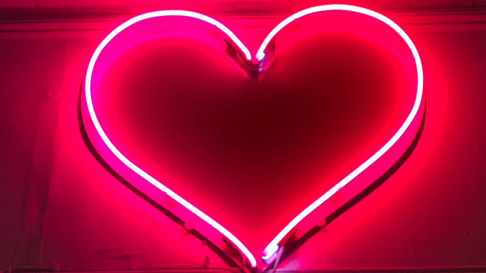 Neon sign of a red heart on a black wall.