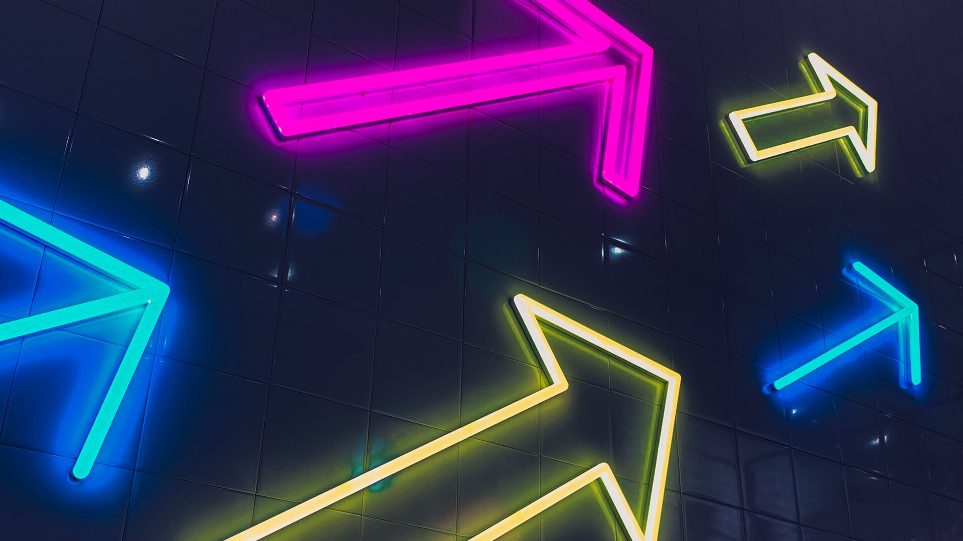 Neon signs of blue, purple and yellow arrows on a black background.