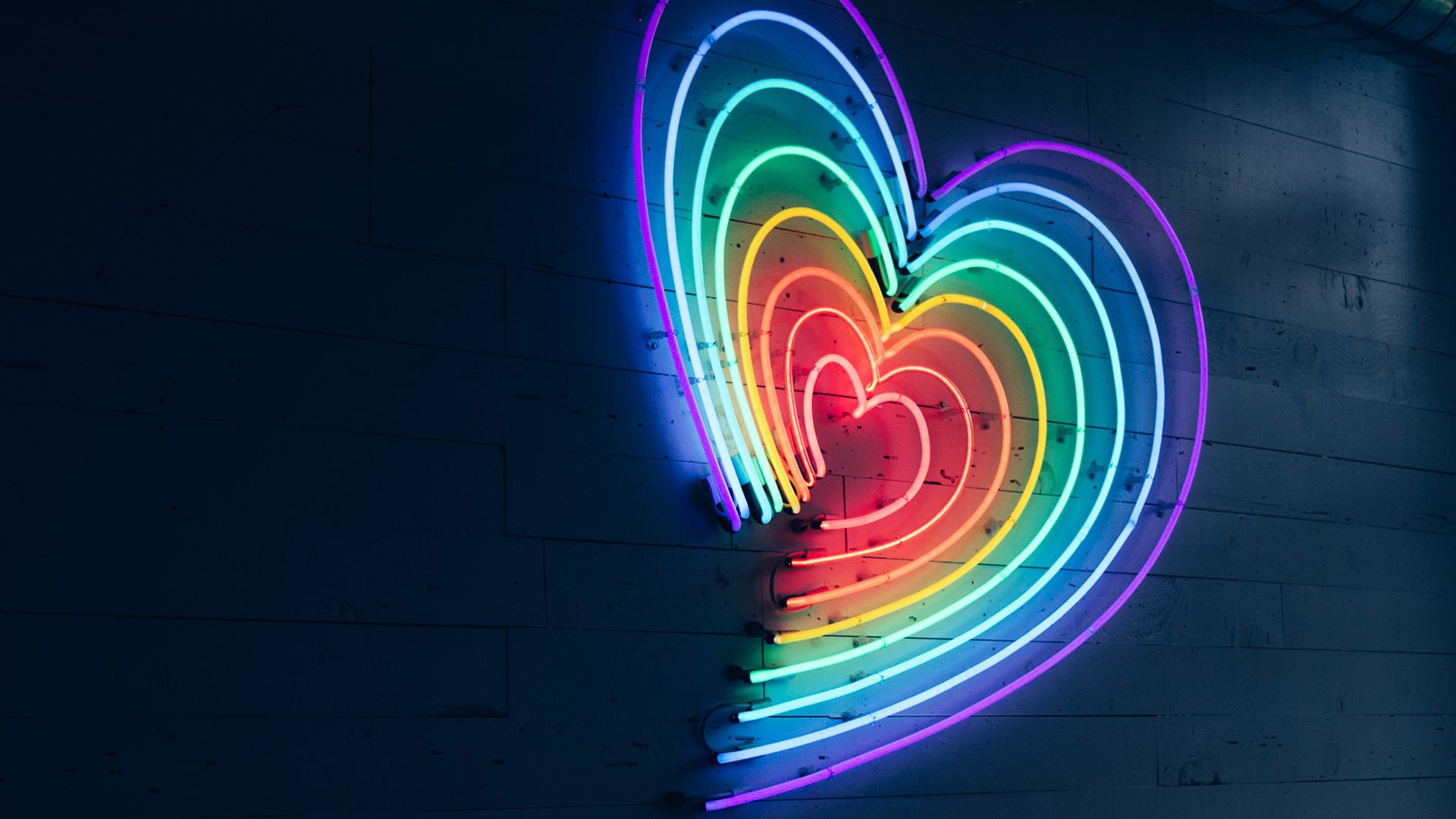 Neon heart sign made from rainbow colours in a black background.
