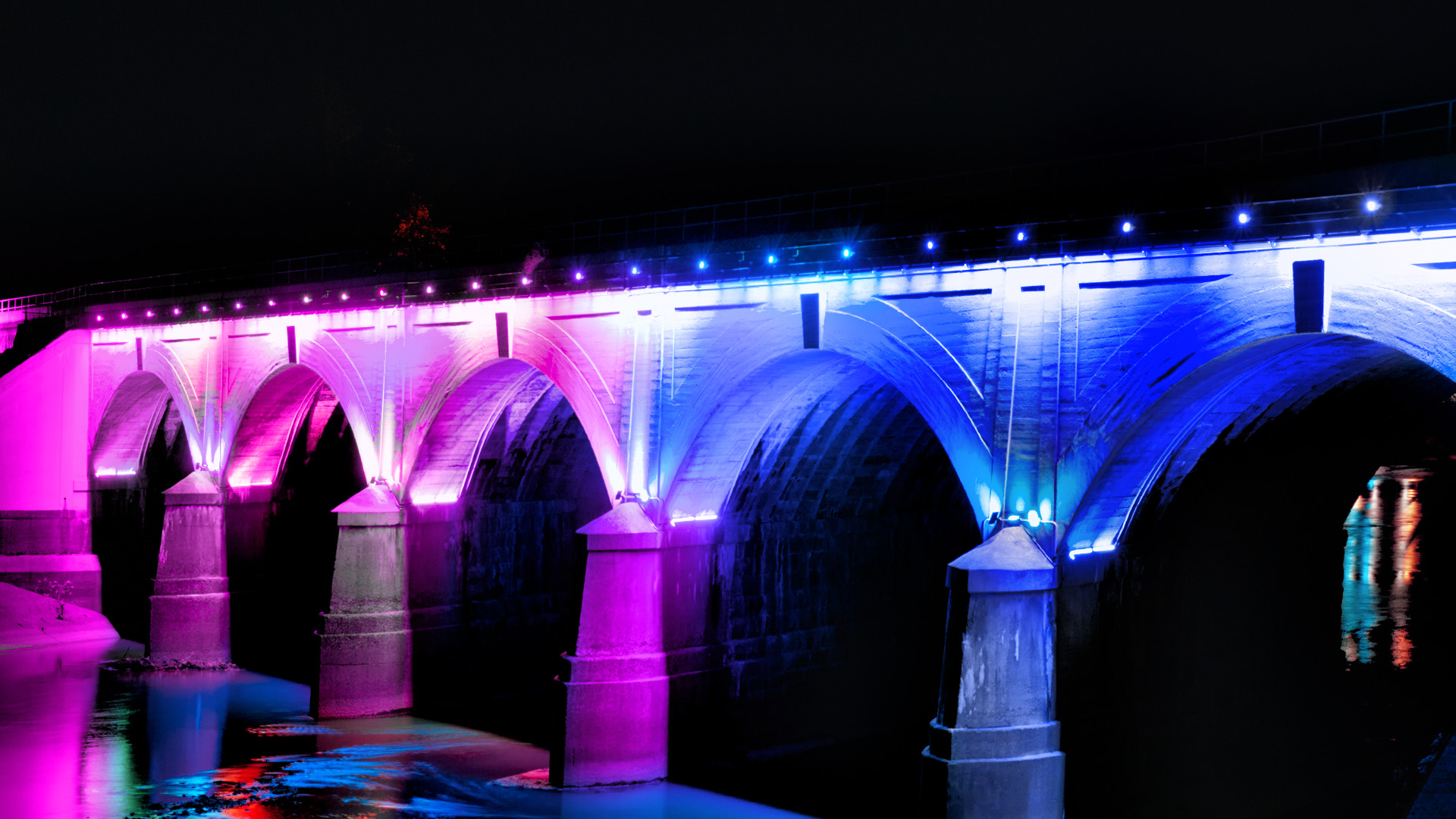 A bridge over water, shinning in neon purple and blue colours.