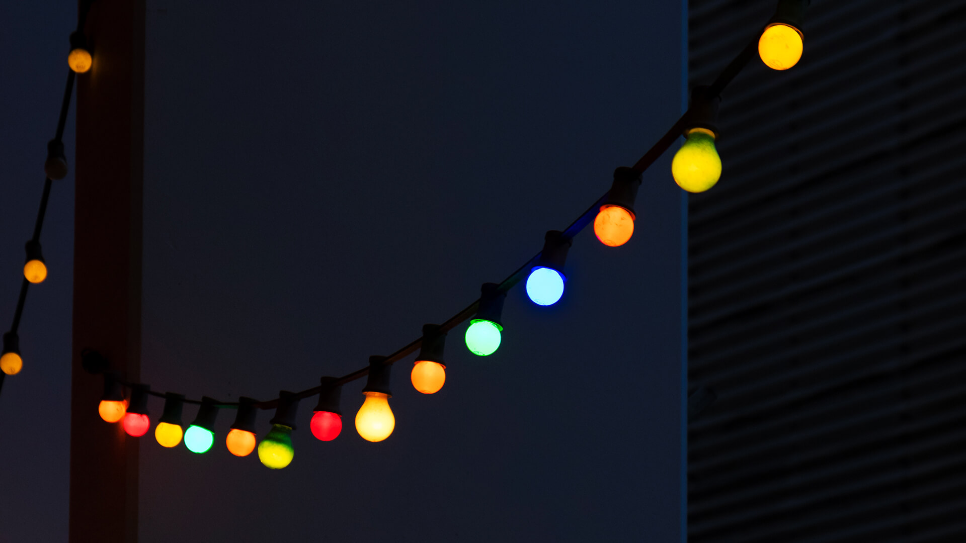 Rainbow coloured lightbulbs on a string at night.